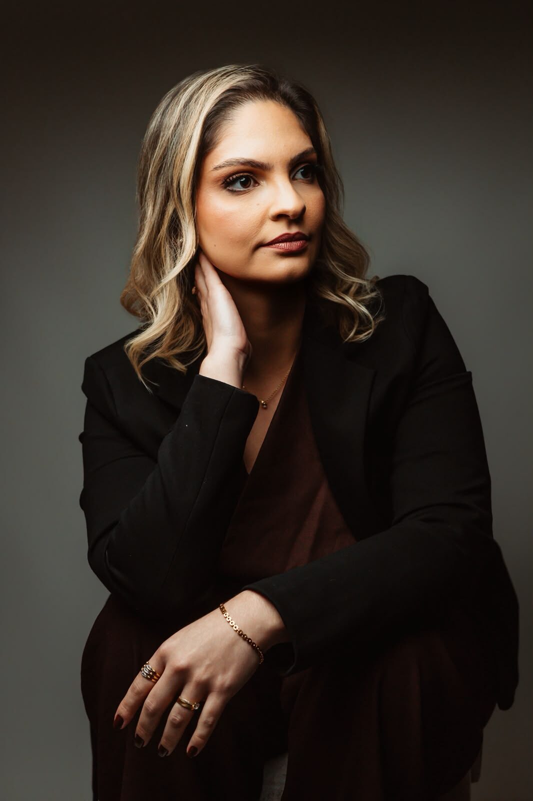 Naãmi Abilhôa de blazer preto, sentada, olhando para o lado